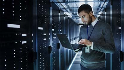 IT-tekniker arbejder på sin bærbare computer i et datacenter fyldt med servere på hylder