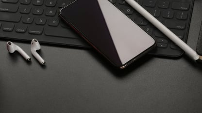 En tablet, mobiltelefon og trådløse hovedtelefoner ligger på et skrivebord.